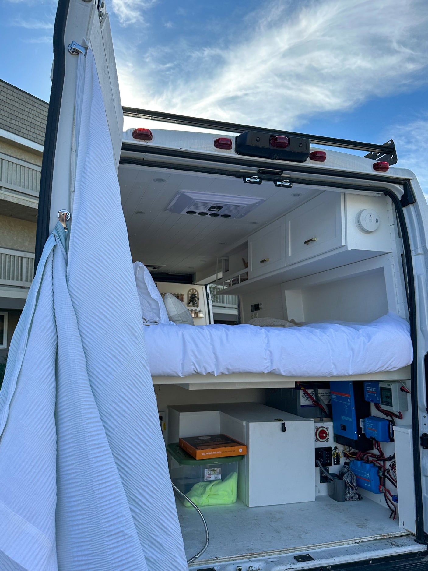 This RV rental's rear view reveals a comfy bed, white ceiling, storage, and exposed electrical system for off-grid power.