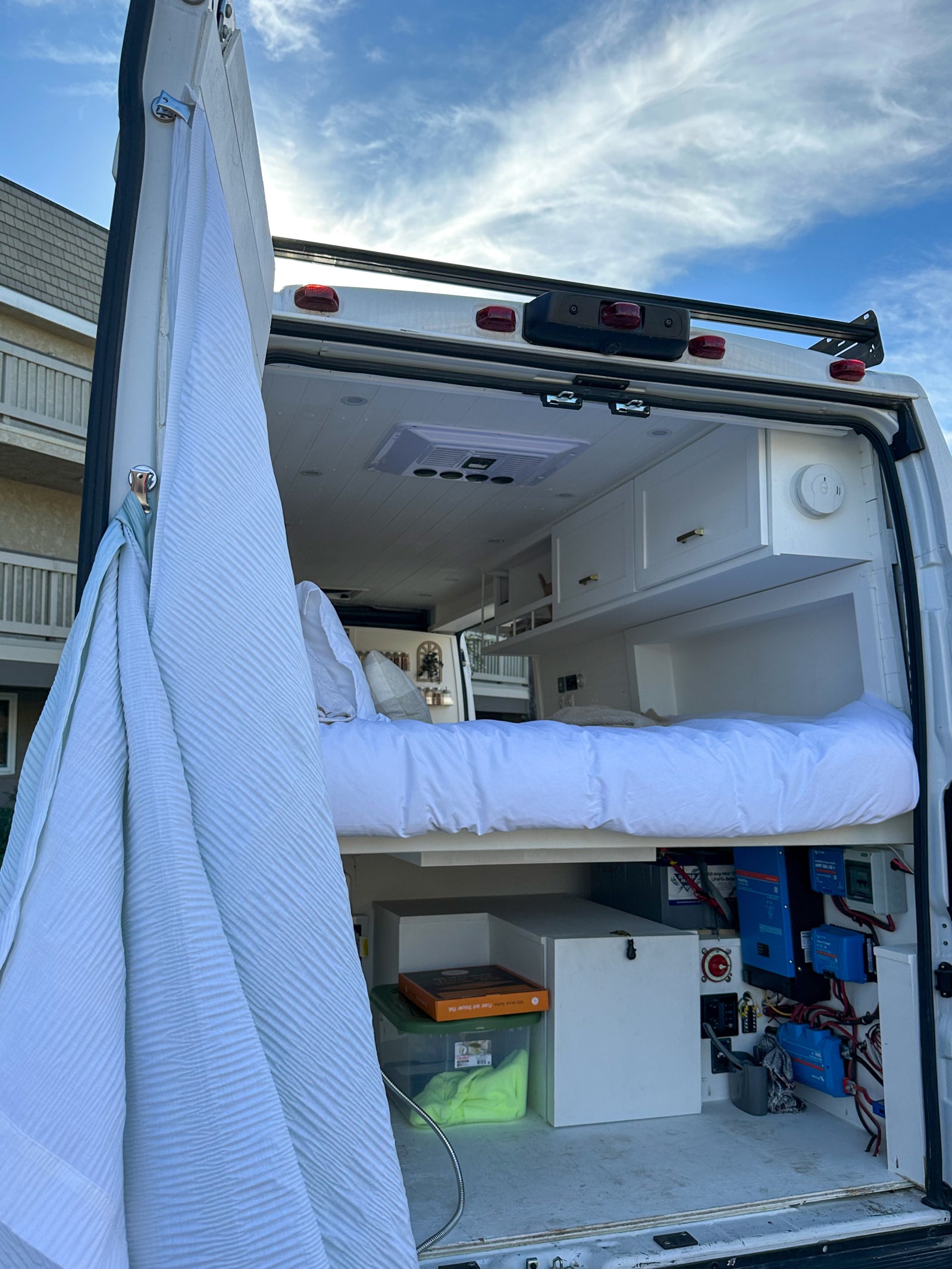 This RV rental's rear view reveals a comfy bed, white ceiling, storage, and exposed electrical system for off-grid power.