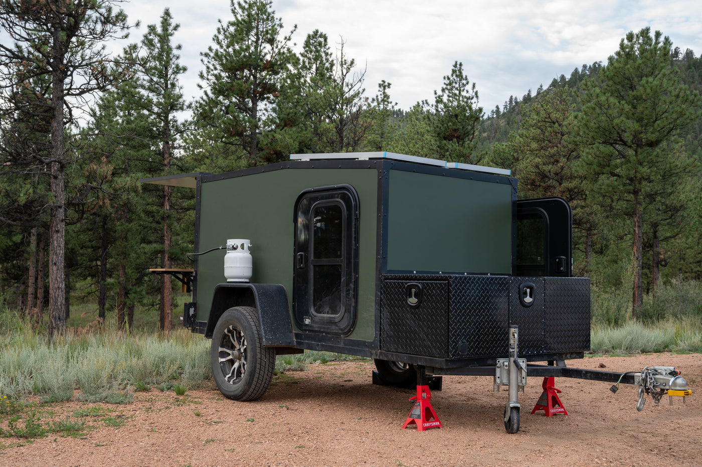 This rugged green camper is ready for your next **RV rental** adventure. Features propane, solar, and storage, set among pine trees. — photo 2