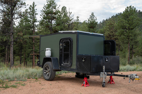 This rugged green camper is ready for your next **RV rental** adventure. Features propane, solar, and storage, set among pine trees.
