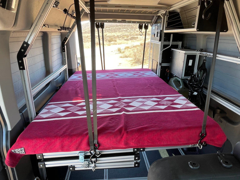 This RV rental showcases a cleverly suspended bed with a red blanket, modular storage, and scenic desert views. — photo 8