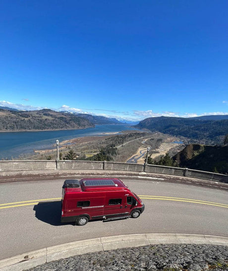 Red RV rental parked at a stunning scenic overlook, offering panoramic views of a wide river valley and mountains.
