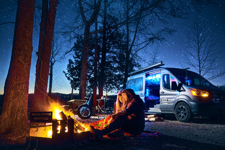 Couple by campfire under starry sky with RV rental camper van. Perfect for nighttime camping adventures.