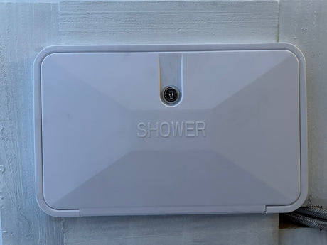 White rectangular exterior shower panel with a keyhole, embossed "SHOWER," for an RV rental.