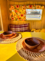 Our charming rv rental offers sunlit dining. Vintage floral curtains, wood paneling, and wooden dishes.