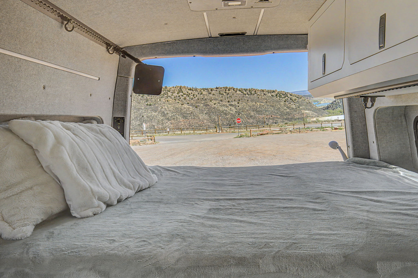 Cozy RV rental camper van bed faces a scenic arid mountain view, ready for travel adventures.