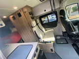 Bright and modern RV rental interior with swiveling front seats, compact kitchen, and rear bed.