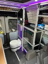RV rental interior with a composting toilet, modular storage system, and vibrant purple accent lighting.