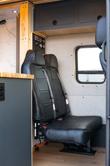 This RV rental features comfortable black passenger seats, a control panel, and an adjacent shower, ideal for travel.