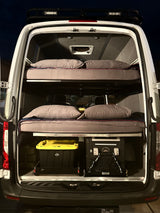 Inside an RV rental camper van: stacked bunk beds with bedding, storage bins, and a portable fridge/freezer for adventure.