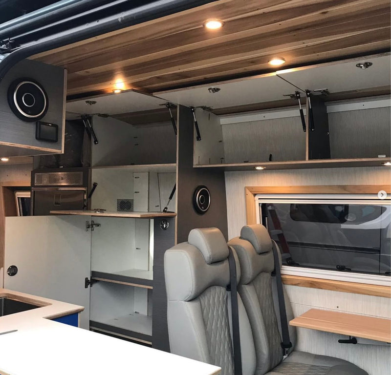 Modern RV rental interior with custom overhead storage, cozy quilted seats, and a functional kitchen. Wood ceiling & window table enhance comfort. — photo 18