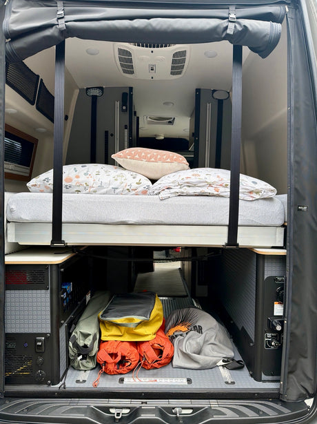 RV rental interior: elevated bed with cozy pillows, and smart storage for camping gear & utility access below. Rolef camper van.