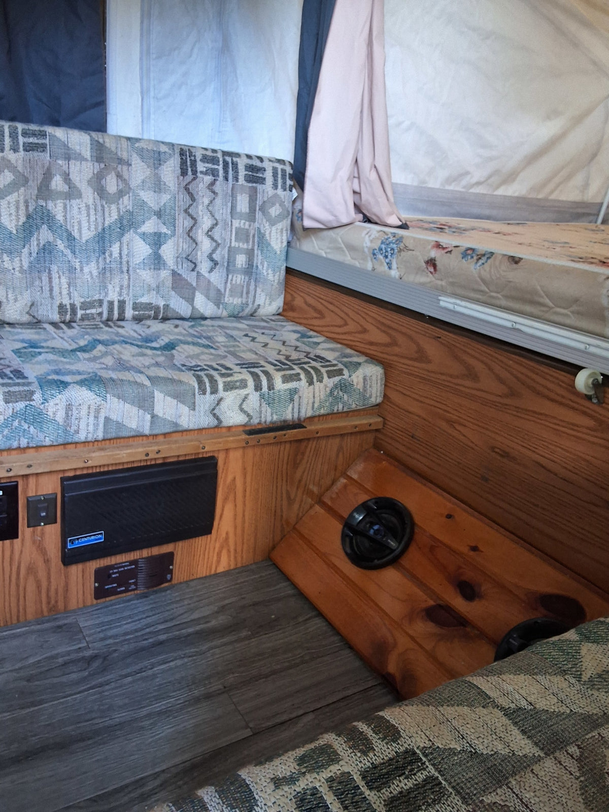 Inside an rv rental: patterned cushions, wood panels, gray flooring, and sleeping area. A compact camper interior. — photo 9