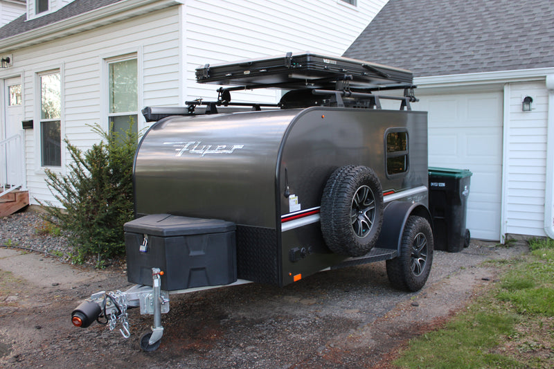 A dark gray Flyer camping trailer, equipped with a rooftop tent, is ready for rv rental adventures, parked on a gravel drive. — photo 6
