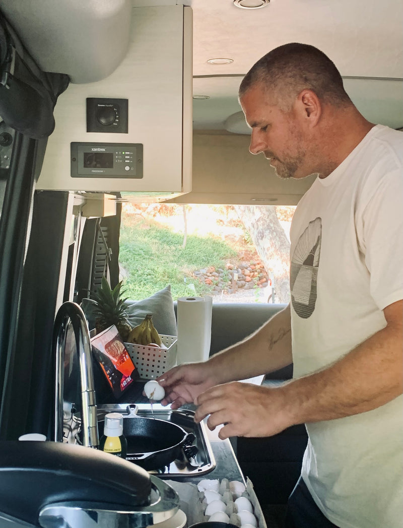 Man cracks egg into pan in a small RV kitchen with controls above. Perfect for an rv rental adventure. — photo 6