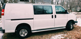 Side view of a white passenger van with tinted windows, parked on ground with leaves & snow. Consider this RV rental.
