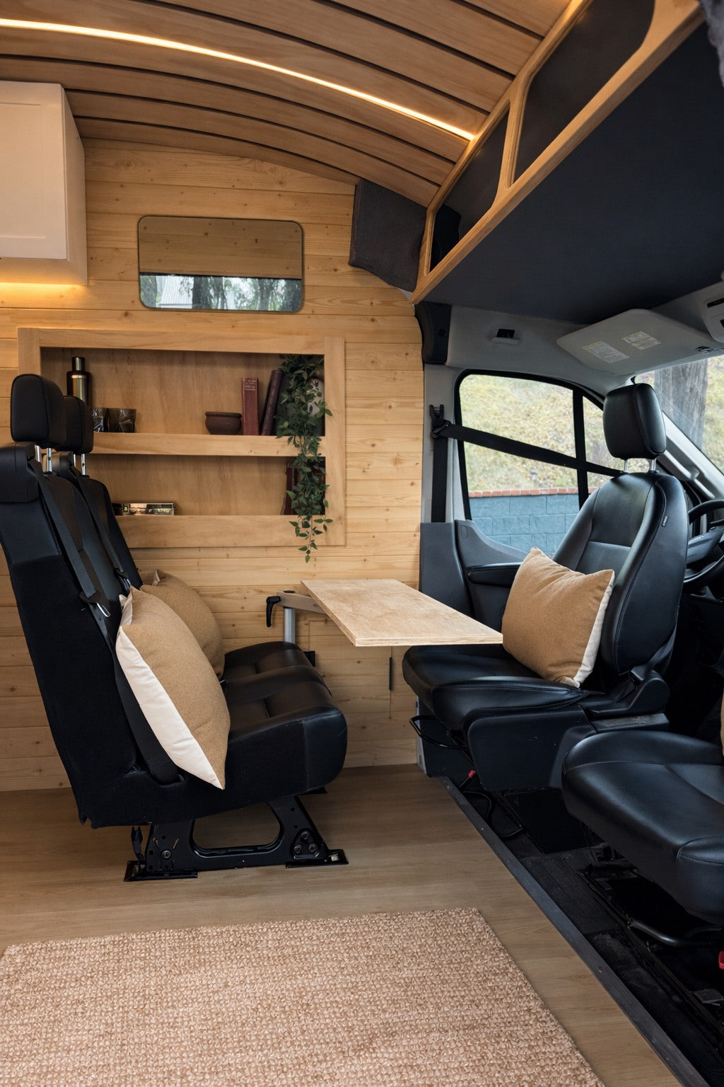 Inside a modern rv rental: wood-paneled walls, comfortable facing seats with a table, and overhead lighting create a cozy dining space.