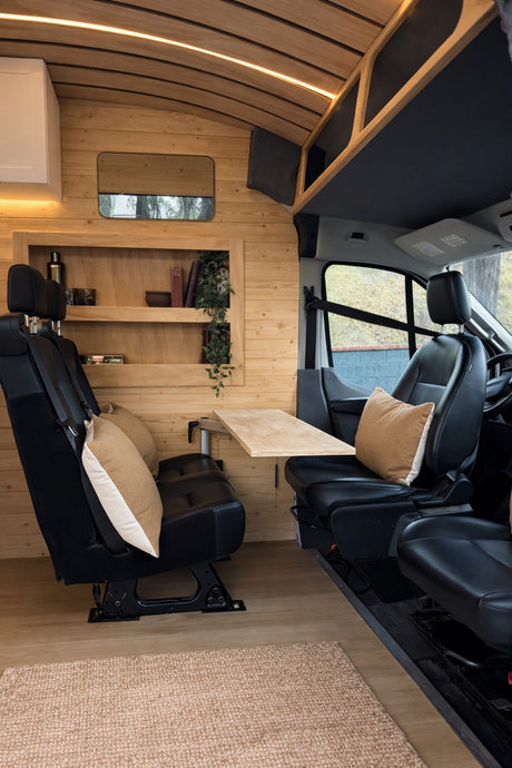 Inside a modern rv rental: wood-paneled walls, comfortable facing seats with a table, and overhead lighting create a cozy dining space.
