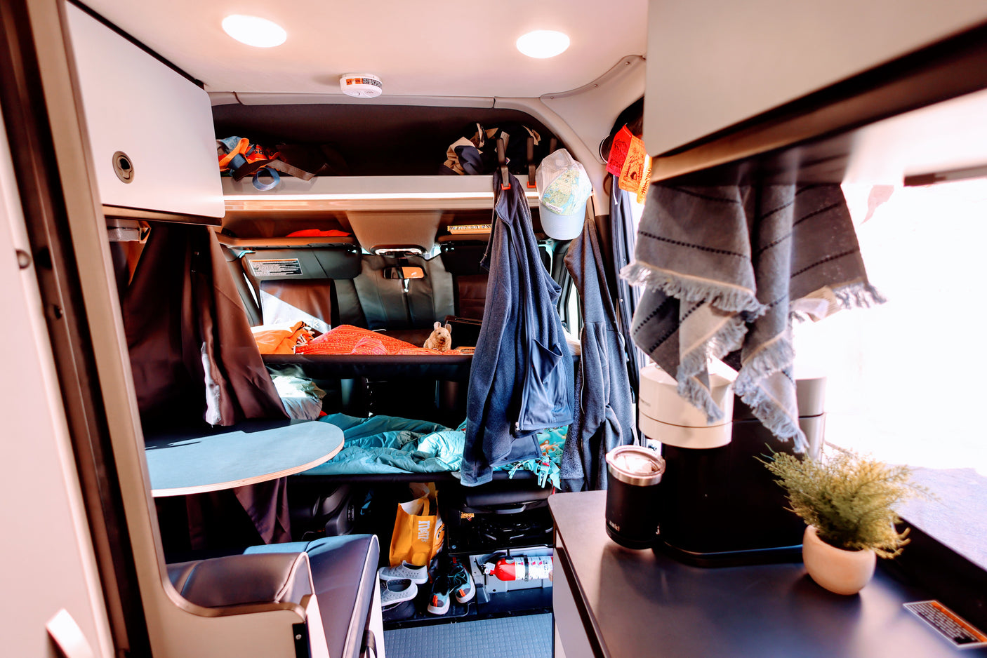 Inside an RV rental: Compact living space with bed, overhead storage, hanging clothes, and a counter with coffee maker.