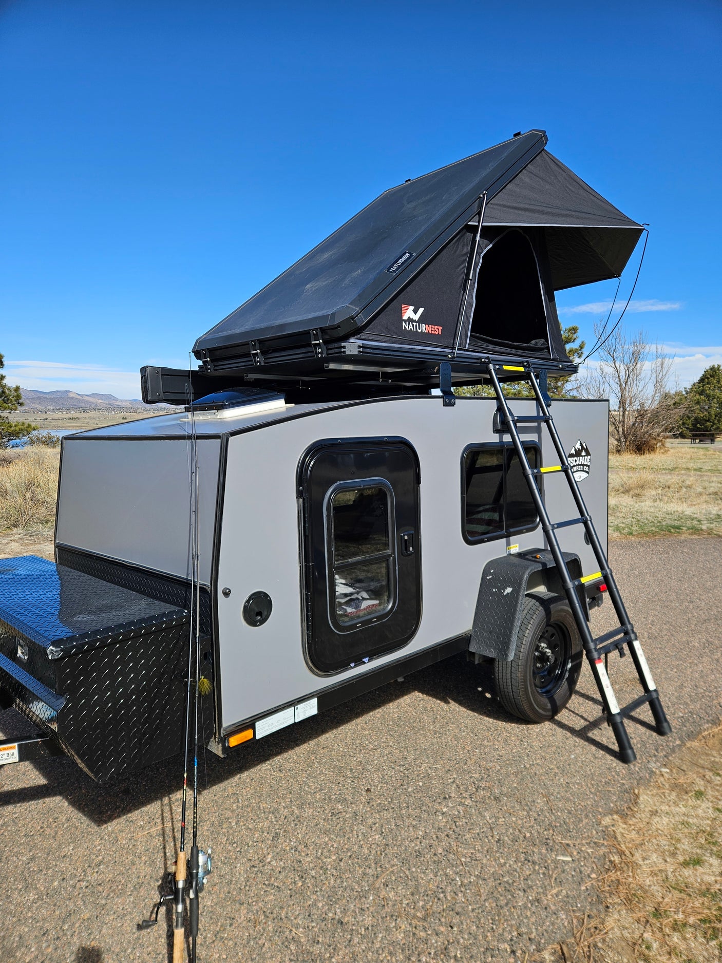 Compact RV rental with a rooftop tent, perfect for outdoor adventures and fishing by the lake.