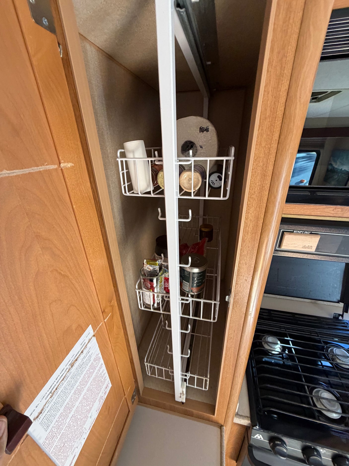 RV rental kitchen: open cabinet with a compact pull-out pantry organizer storing spices and supplies next to the stove.