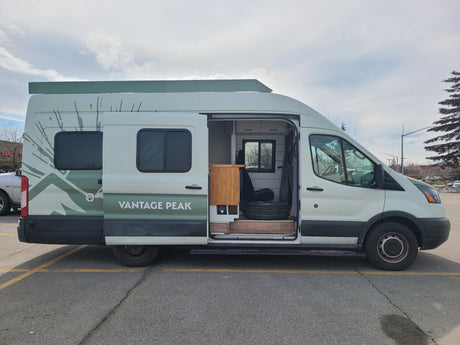 A white Ford Transit camper van conversion, branded 'Vantage Peak', available as an RV rental.