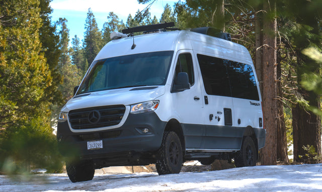 Adventure-ready Mercedes Sprinter camper van for RV rental, parked on snow in a pine forest. Perfect for winter travel.