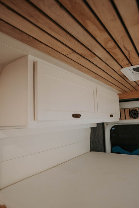 Cozy RV rental interior featuring a slatted wood ceiling, bright white storage cabinets, and a comfortable bed.