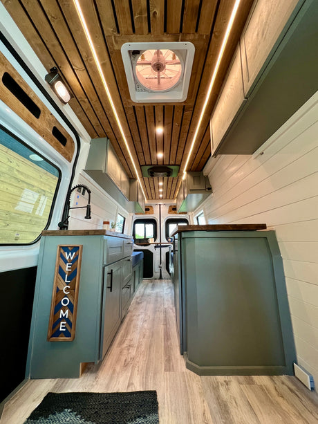 Modern RV rental camper van interior featuring a warm wooden ceiling with LED lights, a functional kitchen area, and adaptable living space.