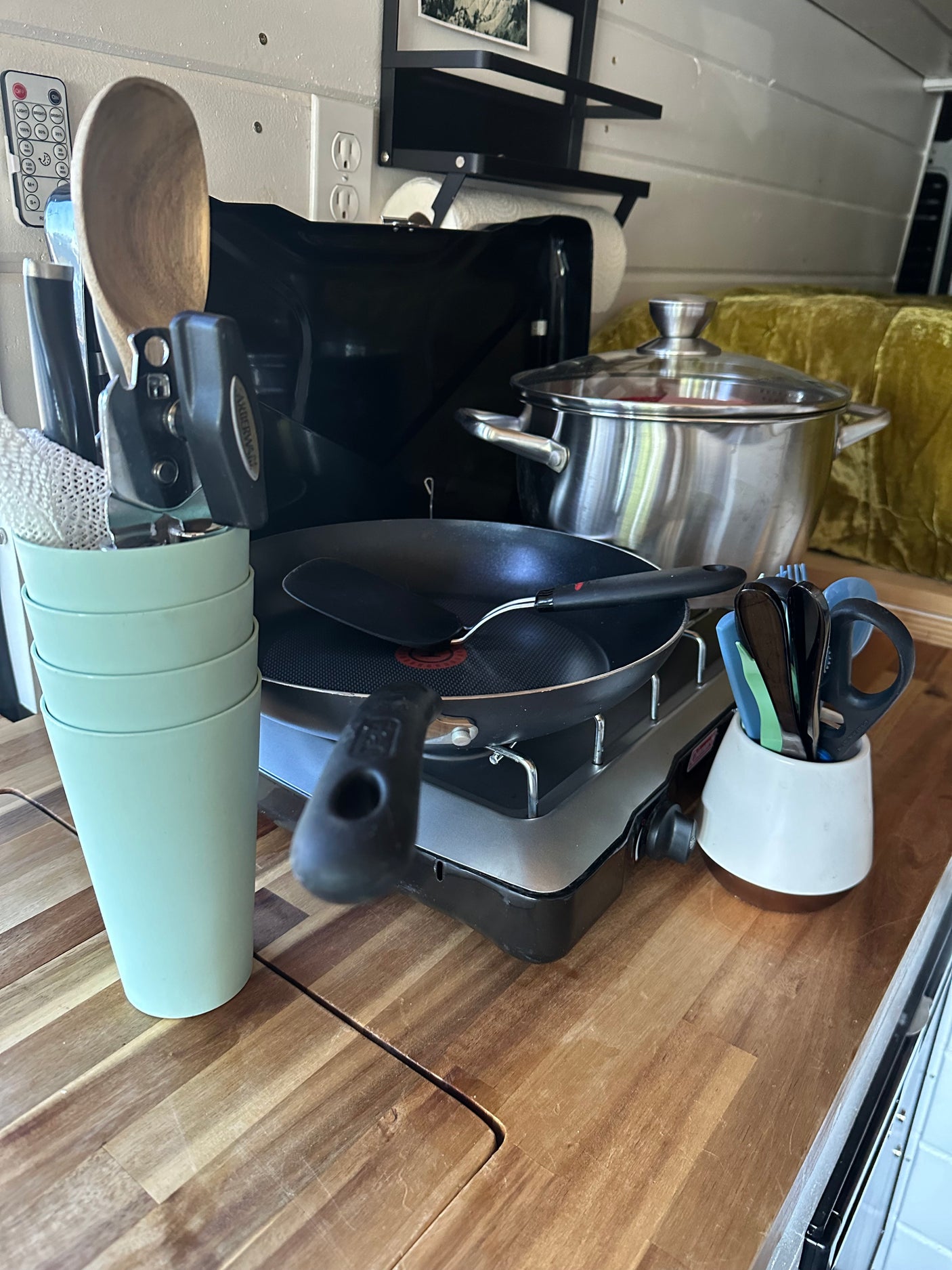 Essential RV rental kitchen tools: portable stove, pots, pan, utensils, and cups on a wooden counter for easy travel cooking.