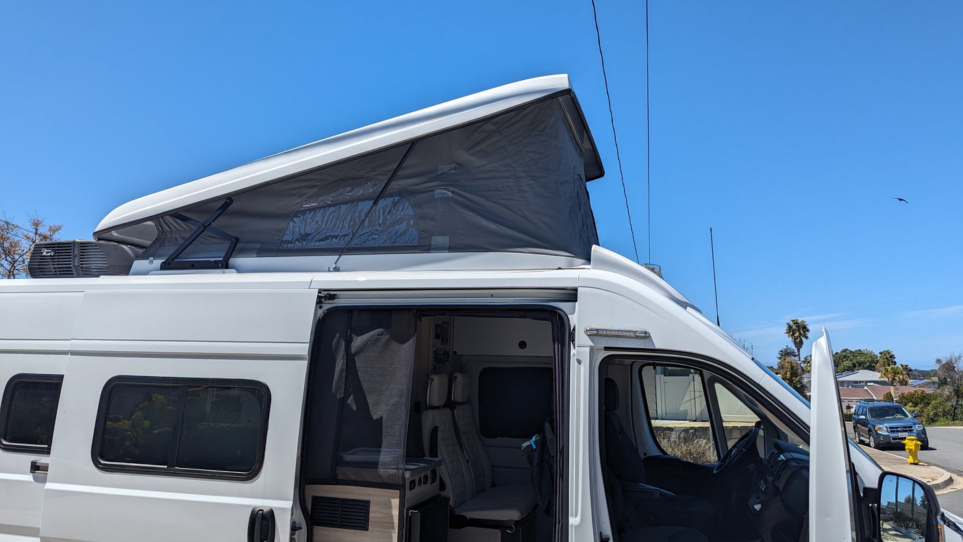 White camper van RV rental with pop-top roof extended. Side door open, revealing interior. Perfect for outdoor adventure.