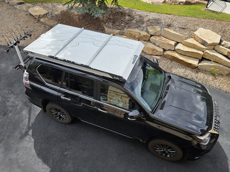 Overhead view of the closed Terrapod RTTx XL mounted on a black SUV, showing the full footprint of the white topo-print lid rack and the low-profile hard shell from above — photo 7