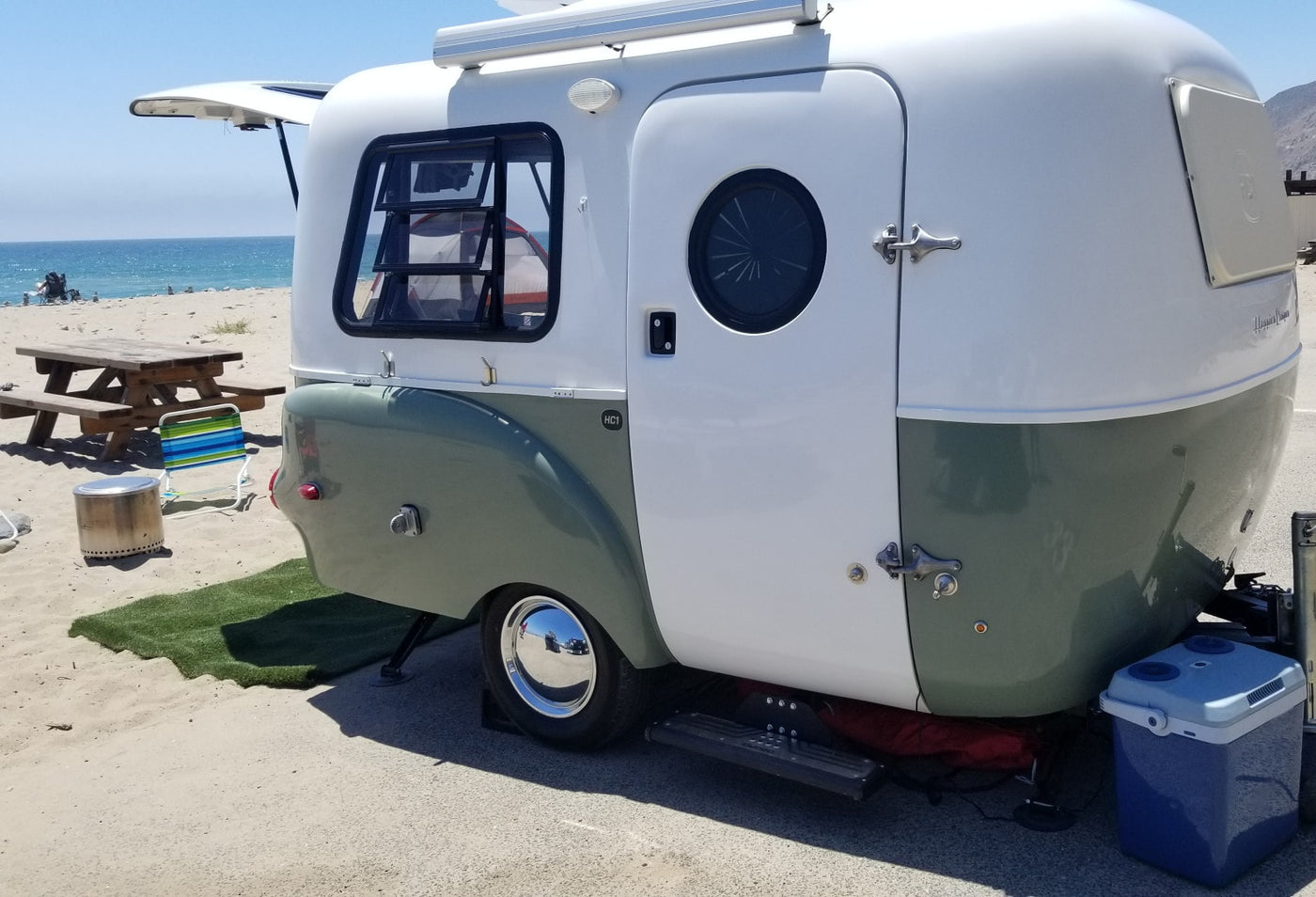 Stylish two-tone RV rental parked on a sunny beach, with a picnic table, cooler, and ocean views. Perfect beach camping setup. — photo 13