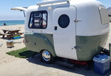 Stylish two-tone RV rental parked on a sunny beach, with a picnic table, cooler, and ocean views. Perfect beach camping setup.
