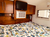 Cozy RV rental interior with a bed, TV, AC, and wooden cabinets. Playful car-themed bedding adds a fun touch.
