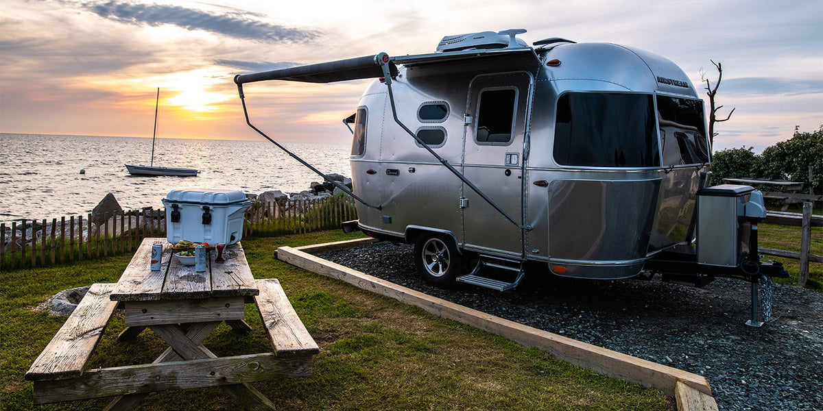 A sleek Airstream RV rental sits oceanside at sunset