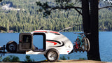 Little Guy teardrop rv rental with bikes by a scenic lake. An open door welcomes you to camping and adventure.