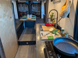 Enjoy cooking and dining in this functional rv rental kitchen with pasta, broccoli, and a cozy table setup.
