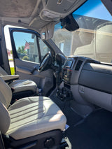 Experience comfort in this RV rental! View of vehicle's roomy interior, light seats, dashboard, and sunlit exterior through windows.
