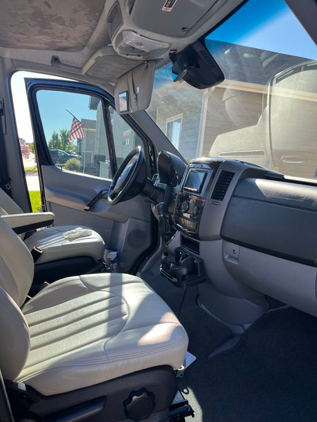 Experience comfort in this RV rental! View of vehicle's roomy interior, light seats, dashboard, and sunlit exterior through windows.