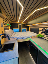 Cozy RV rental interior with a bed, kitchen, and green accent lighting, perfect for van life adventures.