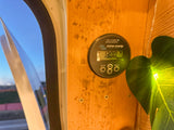 An RV rental interior: A Victron Energy battery monitor shows 13.00V on a wooden wall, next to a window.