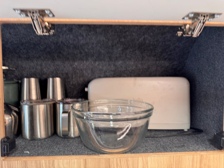 Inside an RV rental cabinet: stainless steel cups, a glass bowl, and a toaster on a felt-lined shelf.