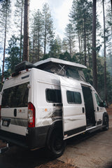 White Winnebago Solis camper van rv rental with pop-top deployed, nestled in a pine forest, ready for adventure.