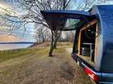 RV rental camper van parked by a serene lake at sunset, with its rear open revealing a cozy interior table setup.