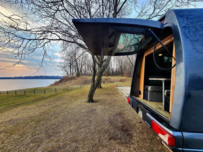 RV rental camper van parked by a serene lake at sunset, with its rear open revealing a cozy interior table setup.