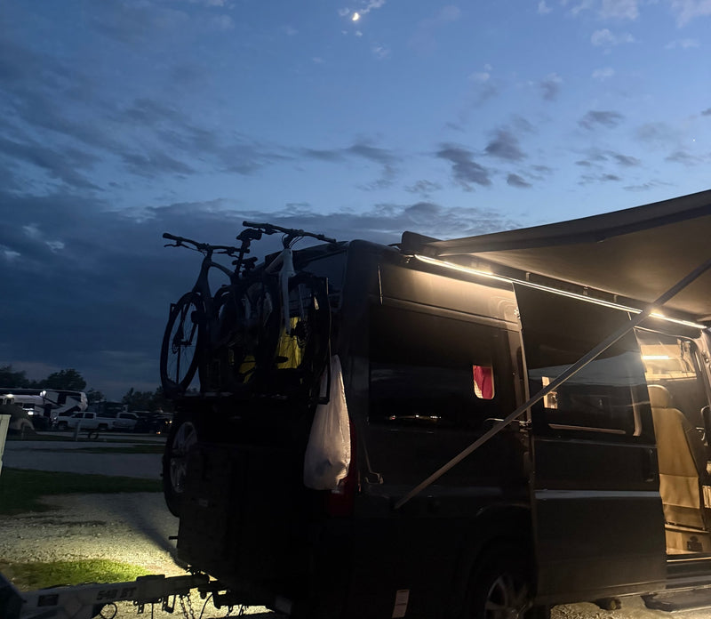 An RV rental at dusk, showcasing bikes on the rear, an illuminated awning, and a crescent moon. Ideal for outdoor adventures. — photo 11