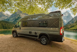 This RV rental is parked by a serene mountain lake, surrounded by lush forest and majestic peaks, ideal for an outdoor adventure.