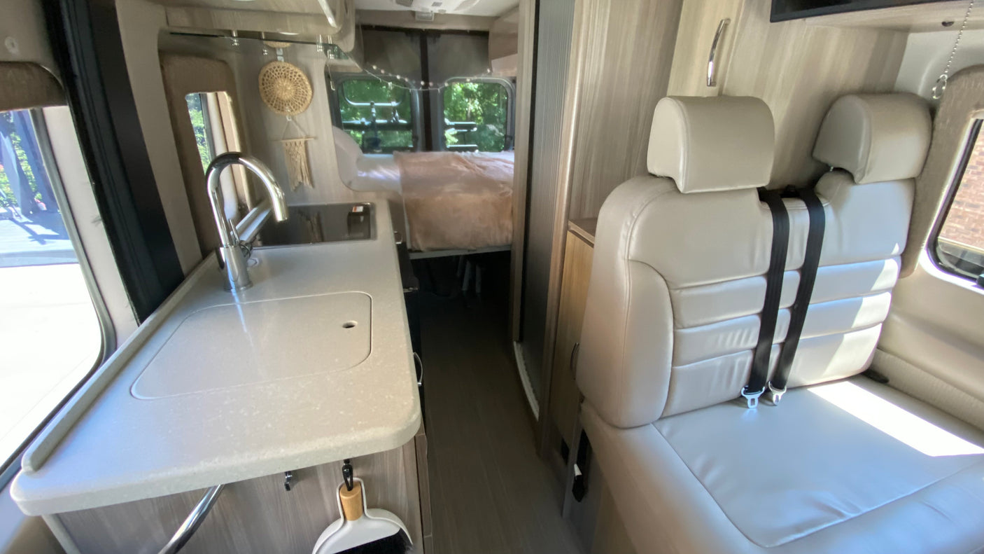 RV rental interior showcasing a modern kitchen with sink, comfortable seating, and a bed area at the rear of the vehicle.