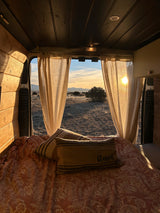 Cozy RV rental interior offers a stunning sunset view over a desert landscape through open back doors, framed by curtains and golden light.